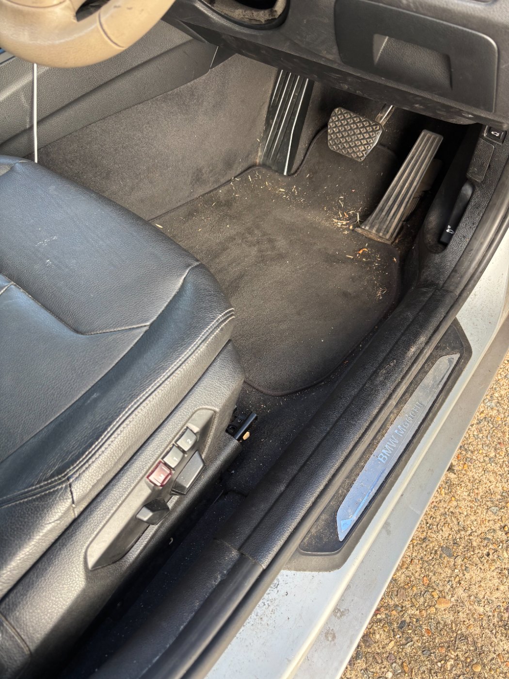 BMW driver footwell before detailing — debris and stained carpet
